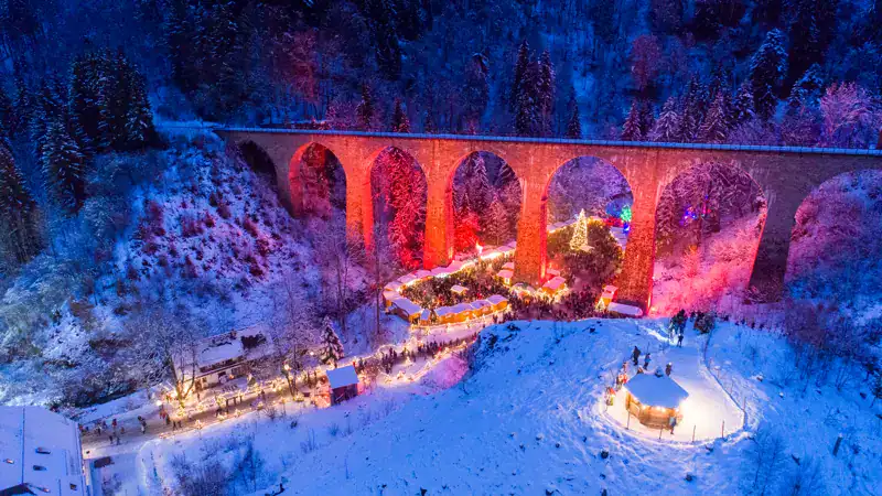 El mercado navideño de la Ravennaschlucht bajo el viaducto iluminado, nevado, desde el aire