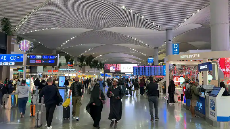 Hall del Aeropuerto de Estambul con pantallas de vuelos y pasajeros con valijas