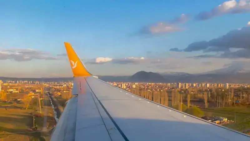 Ala de un avión vista desde la ventanilla, con una ciudad y montañas nevadas de fondo